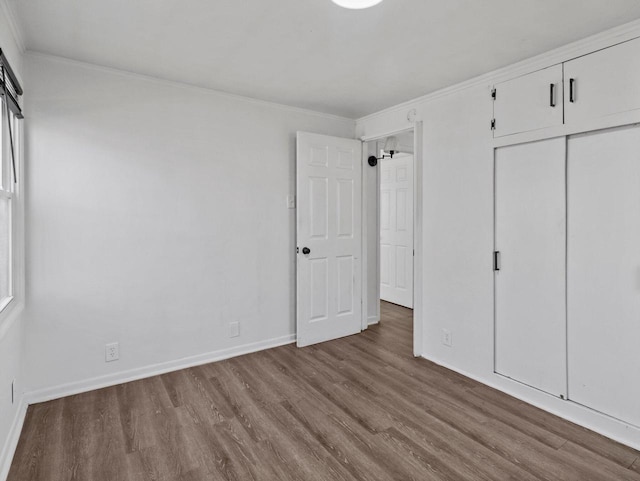 unfurnished bedroom featuring ornamental molding, a closet, wood finished floors, and baseboards