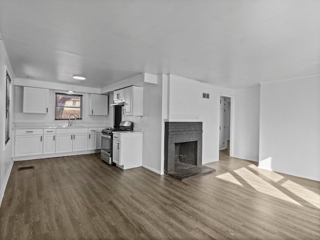 unfurnished living room with a brick fireplace, visible vents, dark wood finished floors, and a sink