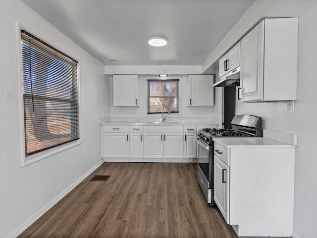 kitchen featuring dark wood finished floors, light countertops, under cabinet range hood, stainless steel range with gas cooktop, and a sink