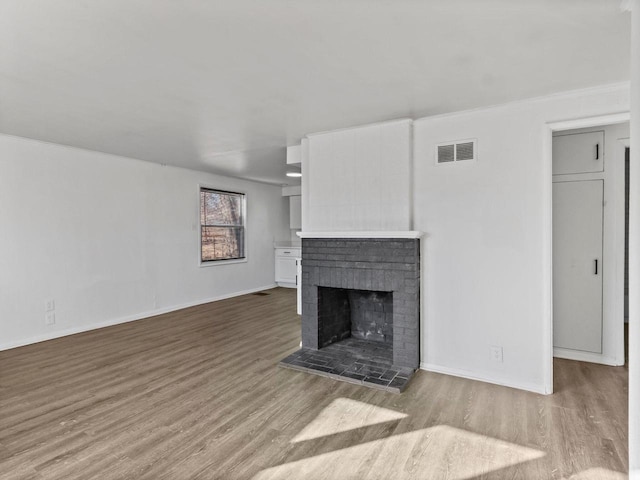 unfurnished living room with a brick fireplace, visible vents, baseboards, and wood finished floors