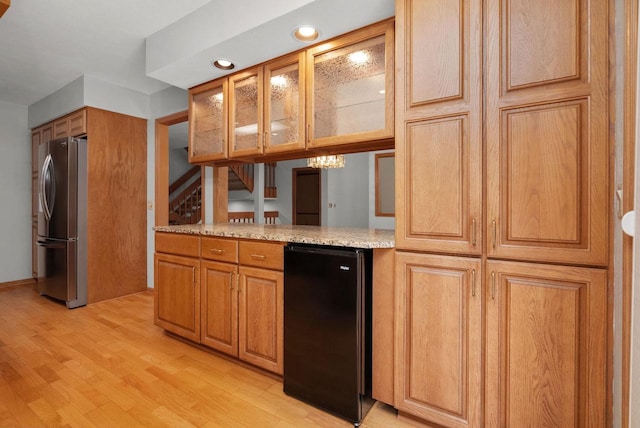 kitchen with light stone counters, refrigerator, light wood-style floors, freestanding refrigerator, and glass insert cabinets