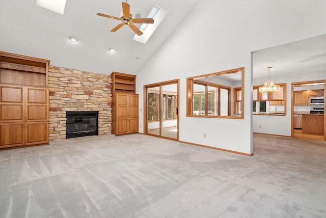 unfurnished living room with a skylight, a fireplace, light colored carpet, baseboards, and ceiling fan with notable chandelier