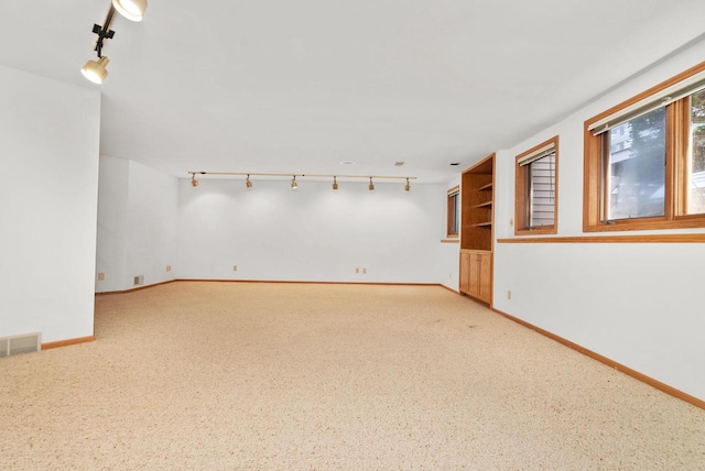 spare room featuring rail lighting, light colored carpet, visible vents, and baseboards