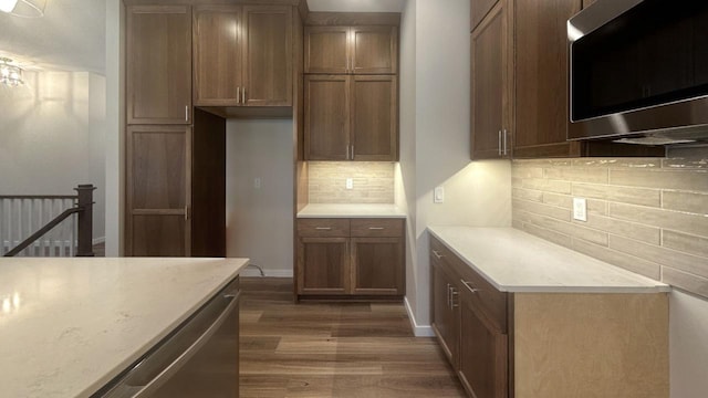 kitchen with dark wood-style floors, light countertops, stainless steel microwave, decorative backsplash, and baseboards