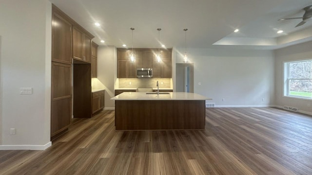 kitchen with a center island with sink, visible vents, stainless steel microwave, a sink, and backsplash