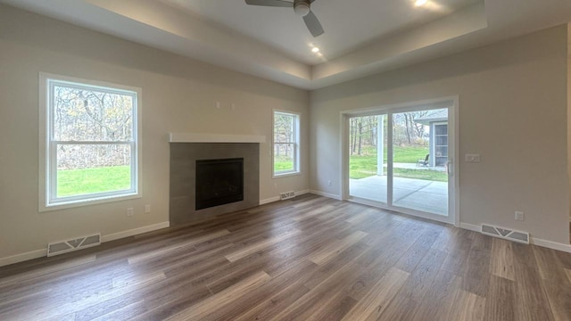 unfurnished living room featuring a wealth of natural light, dark wood-style flooring, a raised ceiling, and visible vents