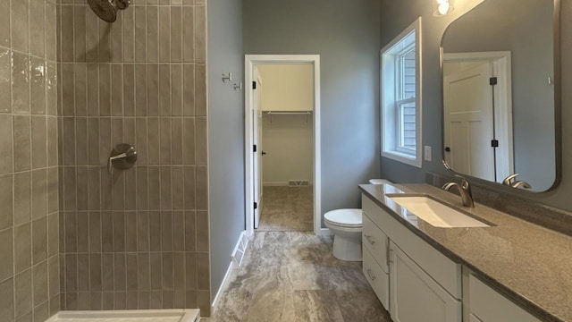 bathroom with visible vents, toilet, a spacious closet, a tile shower, and vanity