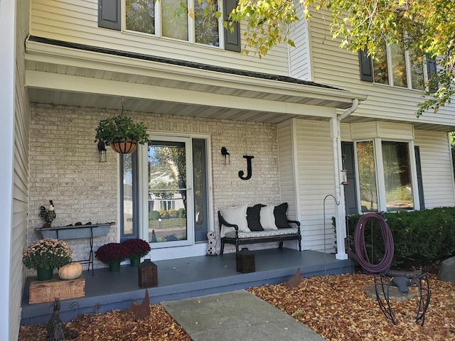 view of exterior entry featuring a porch and brick siding