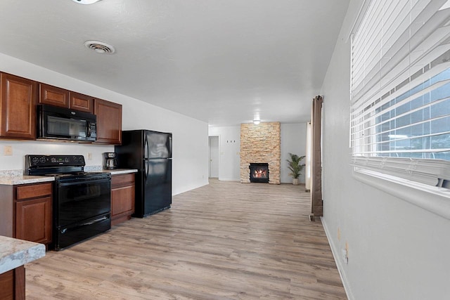 kitchen featuring light wood finished floors, visible vents, light countertops, black appliances, and a fireplace