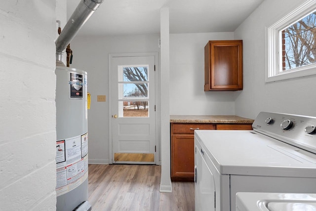 clothes washing area with water heater, a wealth of natural light, light wood-type flooring, and cabinet space