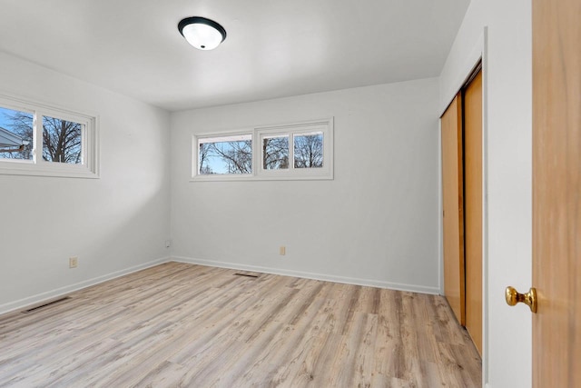 unfurnished bedroom featuring light wood-style floors, baseboards, visible vents, and a closet