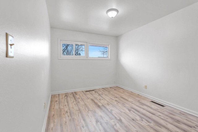 spare room with light wood finished floors, visible vents, and baseboards