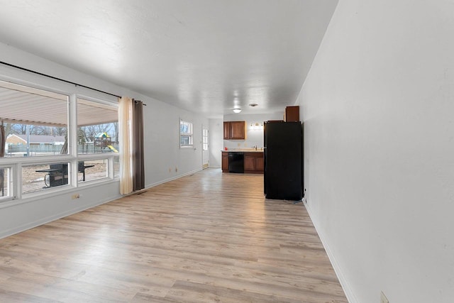 unfurnished living room with a sink, light wood-style flooring, and baseboards