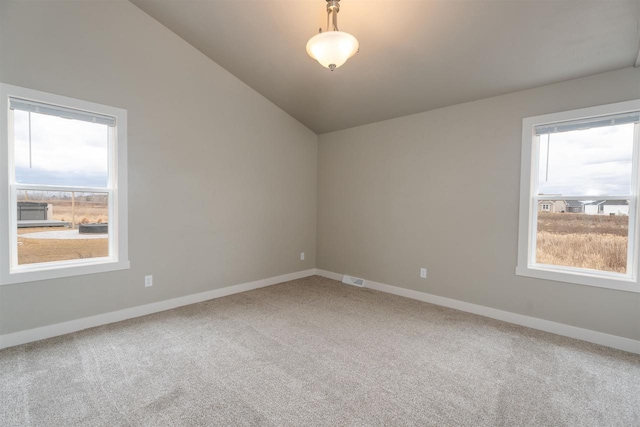 carpeted spare room featuring lofted ceiling and baseboards