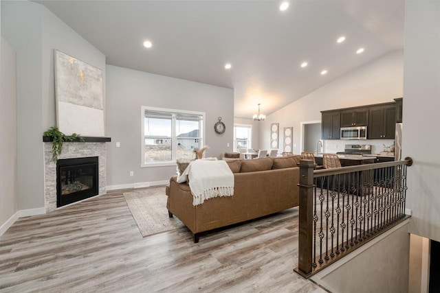 living area featuring light wood-style floors, baseboards, high vaulted ceiling, and a notable chandelier