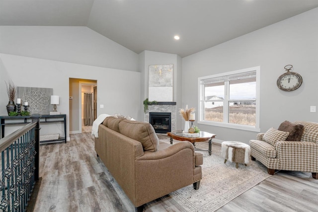 living area with baseboards, vaulted ceiling, wood finished floors, and a glass covered fireplace