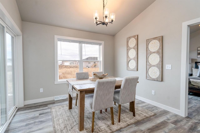 dining area featuring lofted ceiling, an inviting chandelier, visible vents, and wood finished floors