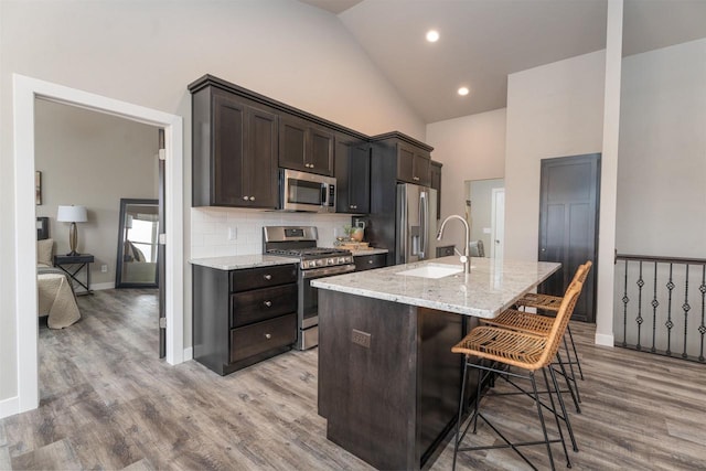 kitchen with light wood finished floors, tasteful backsplash, a kitchen breakfast bar, stainless steel appliances, and a sink