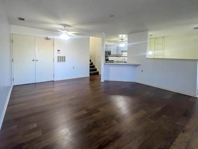 unfurnished living room with dark wood-type flooring, visible vents, ceiling fan, and stairs