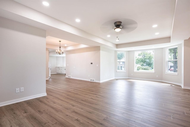 unfurnished living room featuring ceiling fan with notable chandelier, a tray ceiling, baseboards, and wood finished floors