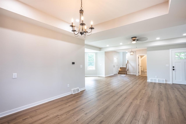 unfurnished living room featuring wood finished floors, stairway, a raised ceiling, and visible vents