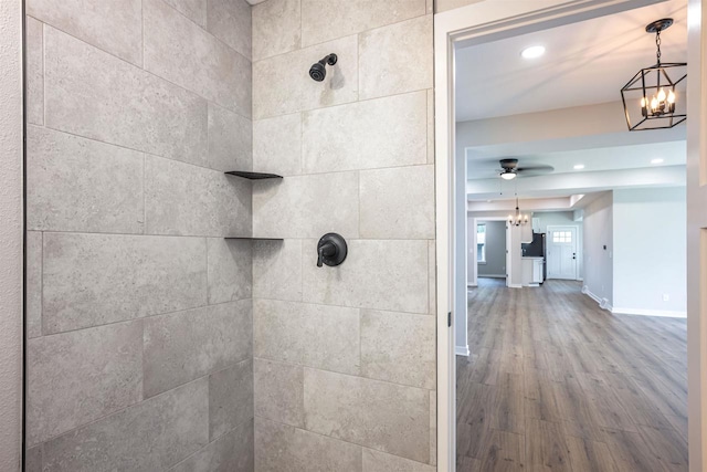 full bathroom featuring recessed lighting, ceiling fan with notable chandelier, wood finished floors, baseboards, and tiled shower