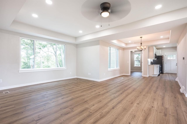 unfurnished living room featuring a wealth of natural light, a tray ceiling, light wood-style flooring, and baseboards