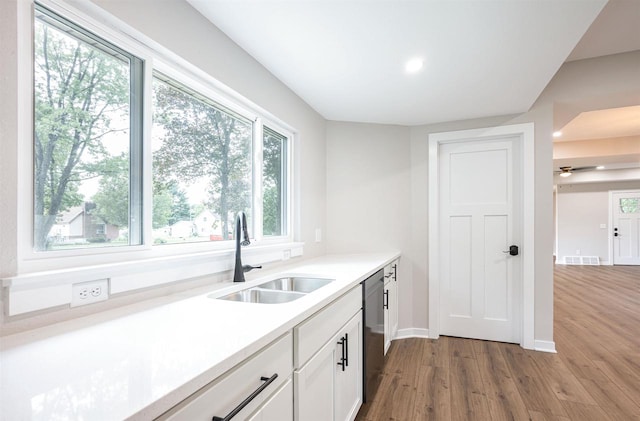 kitchen featuring visible vents, stainless steel dishwasher, white cabinets, a sink, and wood finished floors