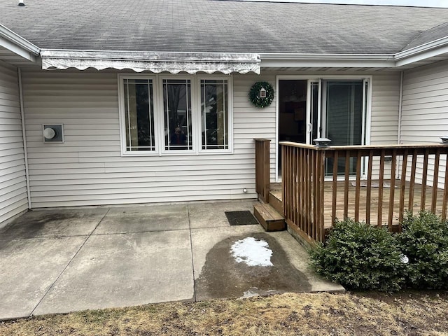 property entrance featuring a shingled roof, a deck, and a patio