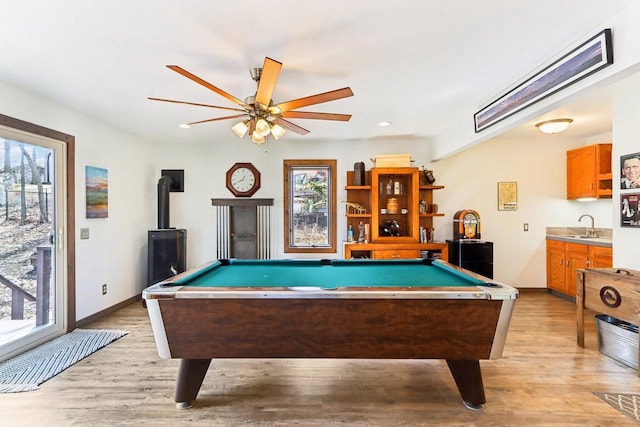 game room with light wood finished floors, billiards, a wood stove, and a sink