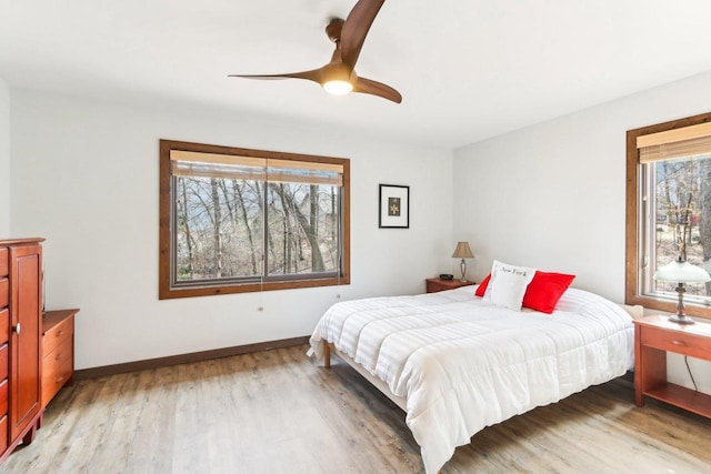 bedroom featuring a ceiling fan, multiple windows, light wood-style floors, and baseboards