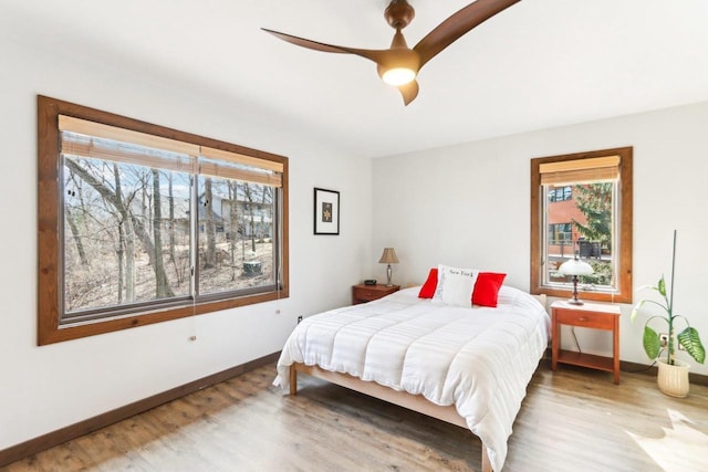 bedroom with ceiling fan, baseboards, multiple windows, and wood finished floors