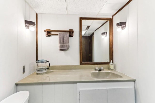 half bath with a drop ceiling, toilet, and vanity