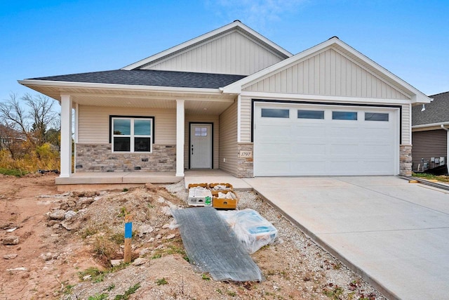 view of front of home with stone siding, covered porch, an attached garage, and concrete driveway