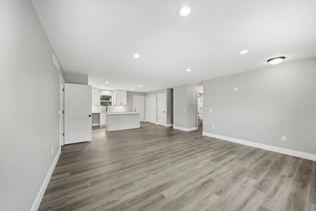 unfurnished living room featuring recessed lighting, a sink, baseboards, and wood finished floors