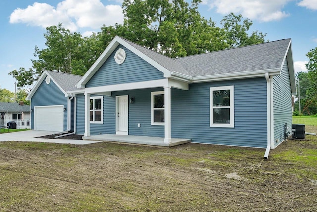 single story home with a porch, central air condition unit, a garage, driveway, and roof with shingles