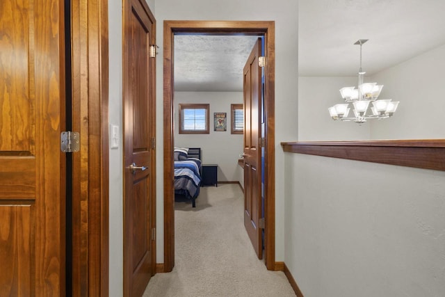 hallway featuring light carpet, a textured ceiling, a chandelier, and baseboards