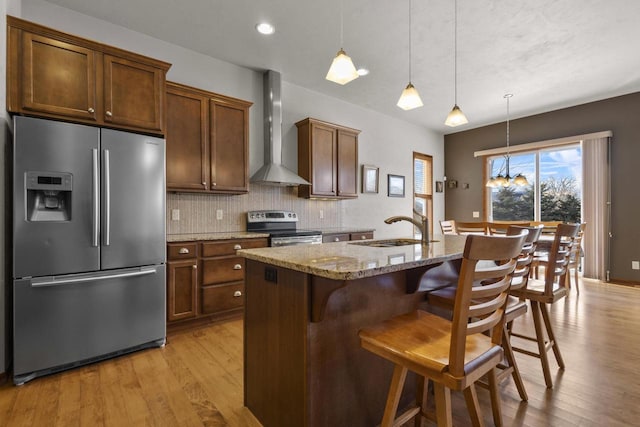 kitchen with light wood-style flooring, stainless steel appliances, a sink, decorative backsplash, and wall chimney exhaust hood