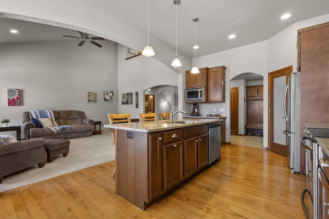 kitchen with arched walkways, stainless steel appliances, open floor plan, a sink, and light wood-type flooring