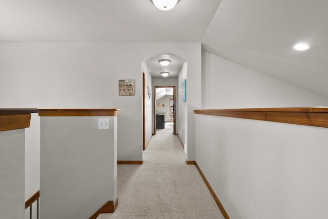 corridor featuring arched walkways, carpet, lofted ceiling, and baseboards