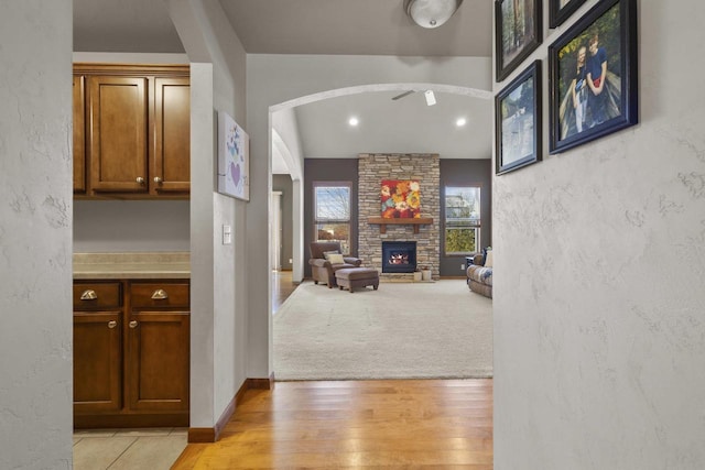 interior space with baseboards, arched walkways, a textured wall, a stone fireplace, and light wood-style floors