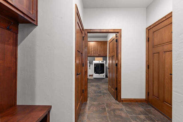 hallway featuring washer / clothes dryer, stone finish flooring, and baseboards