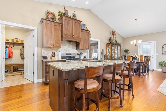 kitchen featuring tasteful backsplash, a center island with sink, lofted ceiling, gas range, and a sink