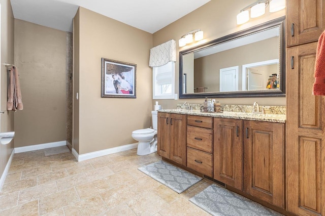 bathroom featuring baseboards, a sink, toilet, and double vanity