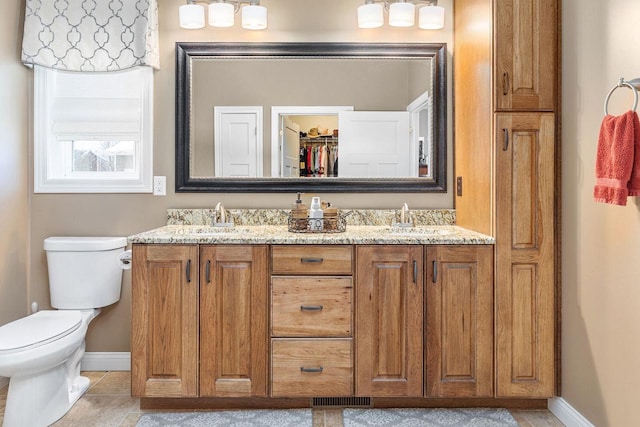 bathroom featuring toilet, double vanity, a closet, and a sink