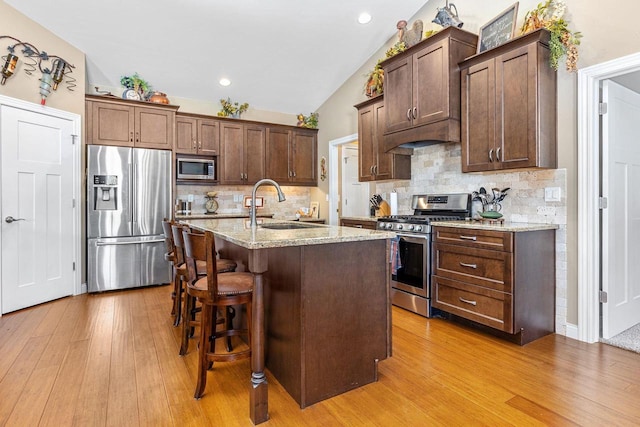 kitchen featuring lofted ceiling, stainless steel appliances, a sink, and light wood-style floors