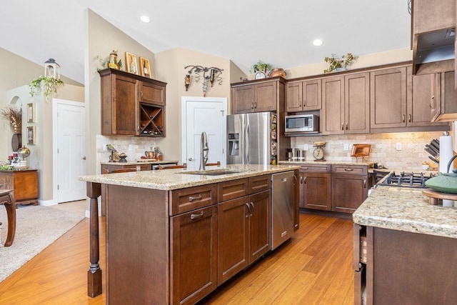 kitchen featuring stainless steel appliances, a kitchen island with sink, a sink, and light wood-style flooring