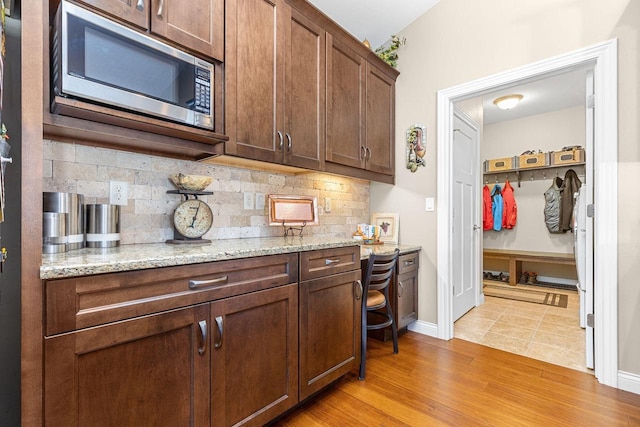 kitchen featuring light stone counters, stainless steel microwave, backsplash, light wood-type flooring, and baseboards