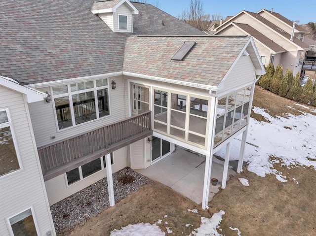 back of property with a shingled roof, a sunroom, and a patio