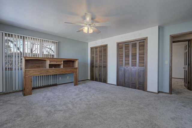 unfurnished bedroom featuring carpet floors, a ceiling fan, baseboards, and two closets